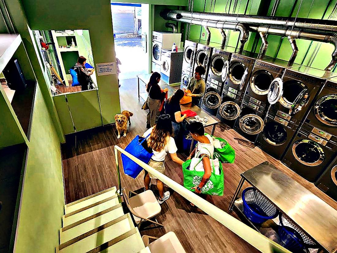 Clientas dentro de Clean Colors con sus bolsas de ropa, junto a las lavadoras